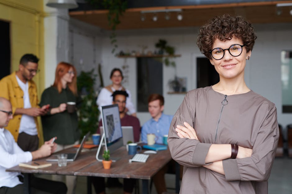 pexels photo 3184405 3184405 Smiling businesswoman with curly hair stands confidently in a modern office space with colleagues.